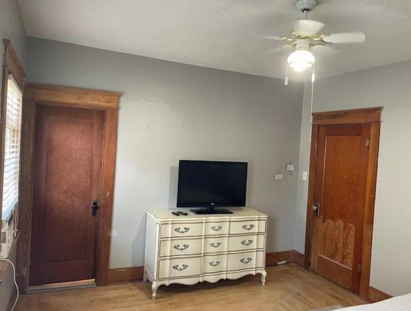 A room with a wooden door, a white dresser with drawers, a ceiling fan, and a television on the dresser. - Porterhouse
(Montpelier)