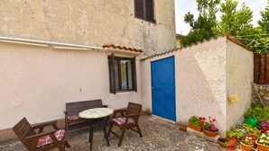 A small outdoor seating area with a table and two chairs, a blue door, and potted plants. - Apartment 2331/111619 (Istria - Fažana), 150m from the beach (Fažana)