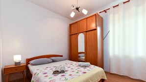 A bedroom with a wooden bed, a nightstand, a ceiling fan, and a window with curtains. - Apartment 2331/111619 (Istria - Fažana), 150m from the beach (Fažana)