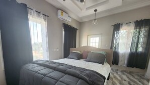 Un dormitorio con cama, ventilador de techo, aire acondicionado y ventana con cortinas.