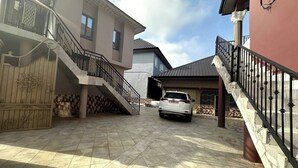 Un barrio residencial con una entrada de coches, un coche blanco estacionado en el centro, y una escalera que lleva a un balcón.