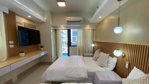 Une chambre d’hôtel avec un grand lit, un téléviseur fixé au mur, un appareil de climatisation et un balcon avec des rideaux.