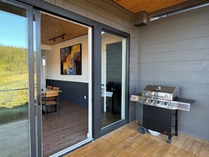 Eine moderne Außenpatio mit einer Schiebetür zu einem Essbereich, einem Grill und Blick auf eine grüne Landschaft.