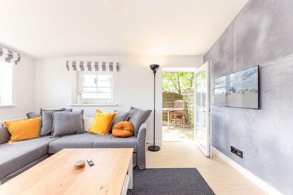 A modern living room with a grey sofa, wooden coffee table, and a view of the garden through a glass door.