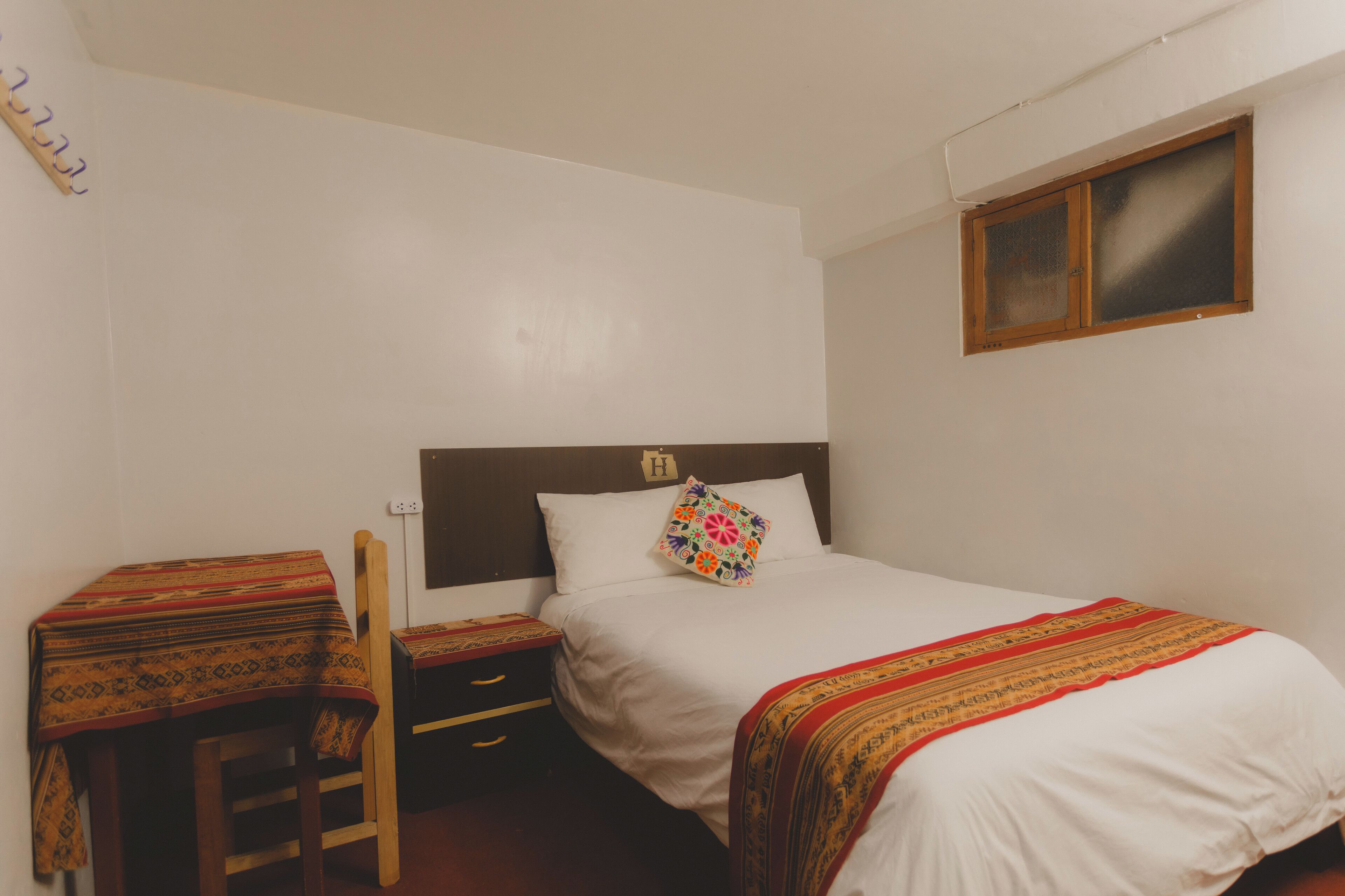 Una cama individual con cabecera de madera, una mesita de noche con lámpara y una ventana pequeña con marco de madera.