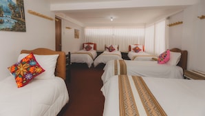 A hotel room with four single beds, each with a distinct patterned pillow. The room has a wooden headboard, a large window with sheer curtains, and a painting on the wall. - Lucios Hostal (Cusco)