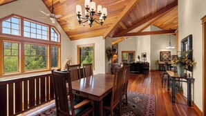 A spacious dining area with a wooden table and chairs, large windows, and a ceiling fan.