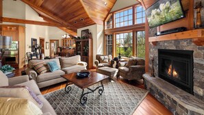 A spacious living room with a fireplace, comfortable seating, and a television mounted on the wall.