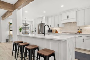 A modern kitchen with white cabinetry, a stainless steel refrigerator, a black faucet, and a large island with bar stools. - Whitewood Oasis-Your Poolside Retreat with  Heated  Pool in Spring, TX  (Spring)