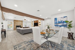 A spacious living area with a glass dining table, white sofas, and a stone fireplace. - Whitewood Oasis-Your Poolside Retreat with  Heated  Pool in Spring, TX  (Spring)