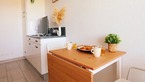 Een kleine keuken met witte kastjes, een houten tafel en een kleine plant in een pot.