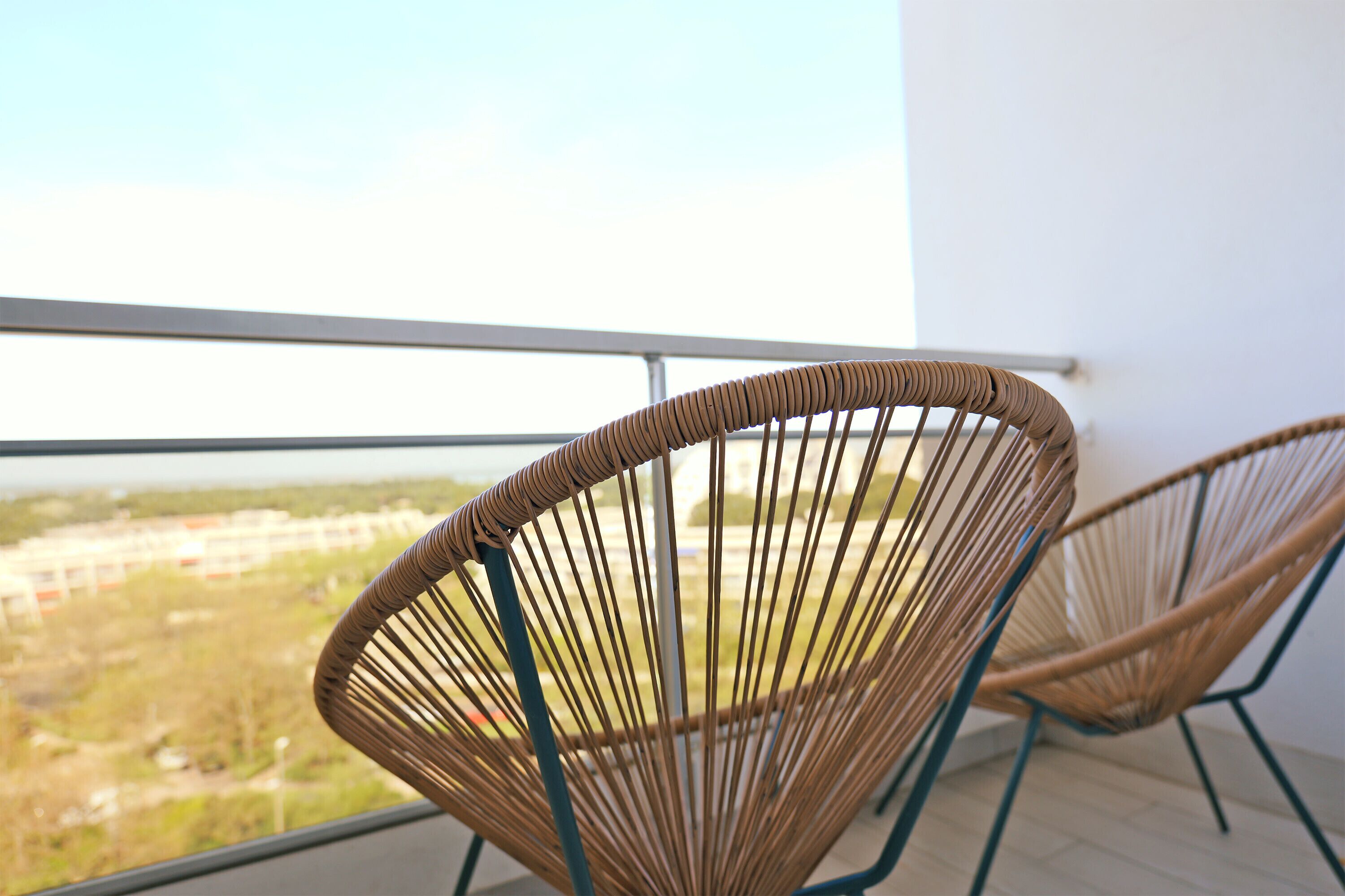 Two wicker chairs with metal frames on a balcony with a view of a distant landscape.