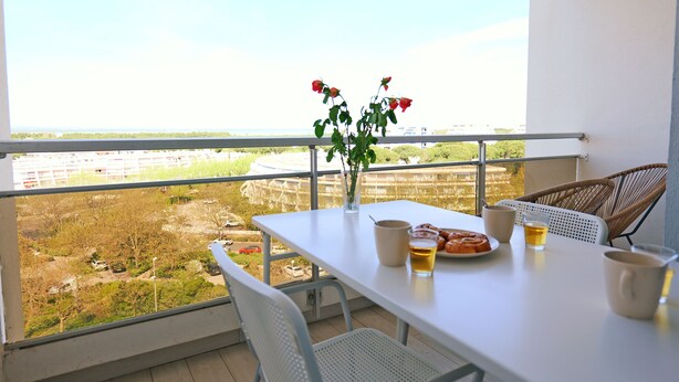 Een balkon met een tafel, stoelen, een bloevas en uitzicht op de stad.