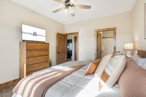 Une chambre à coucher avec un lit, un ventilateur de plafond, un téléviseur fixé sur un meuble en bois et un panneau avec un logo.