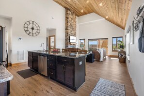 A spacious kitchen with a central island, a stone accent wall, and a large clock on the wall. - Lake Lookout Retreat with Private Hot Tub, Free Attraction Tickets & Community Pools (Branson)