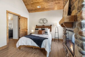 Ein Schlafzimmer mit Holzbalkendecke, einem Steinkamin, einem Bett mit weißer Daunendecke und einem Nachttisch mit Lampe.