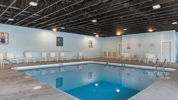 An indoor swimming pool with a blue floor, surrounded by white chairs and a lifeguard station.