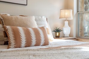 A bed with patterned pillows, a bedside lamp, and a small plant on a nightstand. - Lake Lookout Retreat with Private Hot Tub, Free Attraction Tickets & Community Pools (Branson)