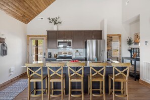 Une cuisine moderne dotée d’un îlot central, de chaises en bois et d’appareils électroménagers en acier inoxydable.