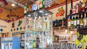 A bar area with a glass display case, shelves with bottles, and a blue cooler. - Touch the Wind (Sap Yai)