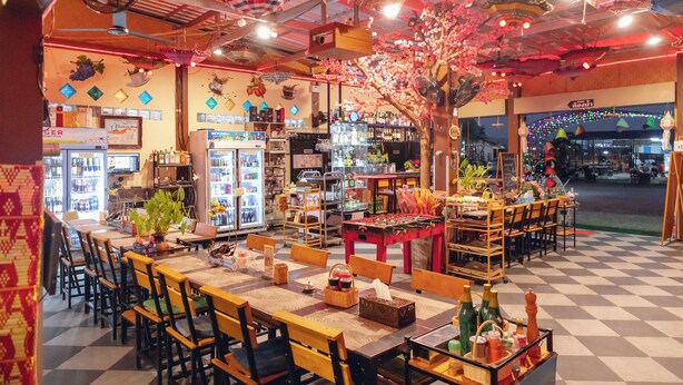 A restaurant with a checkered floor, wooden tables and chairs, and a variety of food and drink displays. - Touch the Wind (Sap Yai)