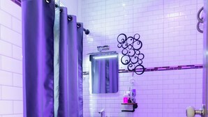 A bathroom with a toilet, sink, and shower area, featuring white tiled walls and a geometric patterned floor. - Touch the Wind (Sap Yai)