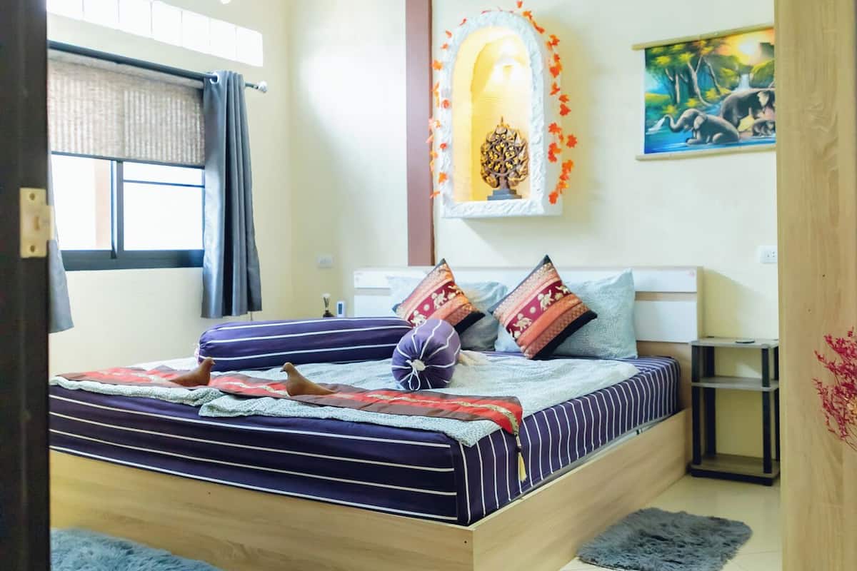 Une chambre à coucher avec un lit, une table de chevet, une lampe, une fenêtre avec des rideaux et un tableau au mur.