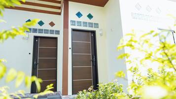 Une entrée d’immeuble avec deux portes, un mur recouvert de carreaux orné d’éléments décoratifs et un petit jardin avec des plantes.