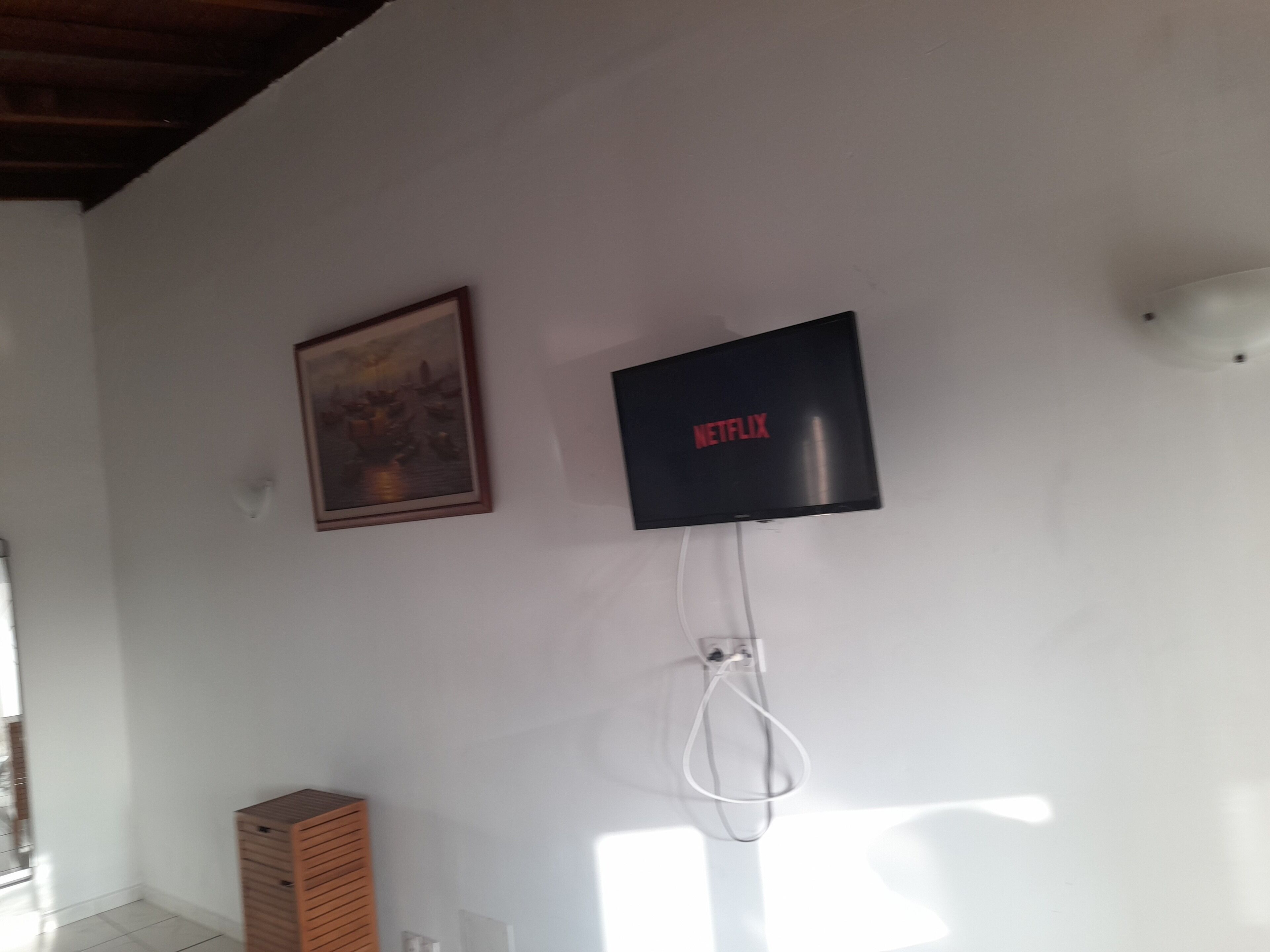 A wall-mounted TV with a Netflix logo, a framed picture, and a white wall socket.