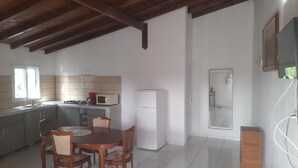 A kitchen with a dining table and chairs, a microwave, a refrigerator, and a window. - Sunset inn (Sainte-Anne)