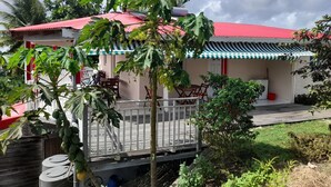 A house with a red roof, a covered porch, and a garden with various plants. - Sunset inn (Sainte-Anne)