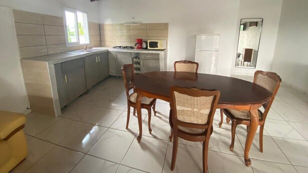 A spacious dining area with a wooden table and chairs, a kitchen with modern appliances, and a large mirror on the wall. - Sunset inn (Sainte-Anne)