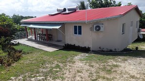 A single-story house with a red roof, a covered patio with a table and chairs, and an air conditioning unit mounted on the wall. - Sunset inn (Sainte-Anne)