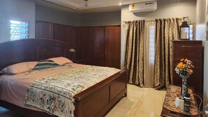 Une chambre à coucher comprenant un lit, un ventilateur de plafond, un appareil de climatisation, des rideaux, une table de chevet et une lampe.