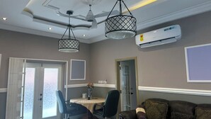 Un salon moderne avec un coin repas, doté d’un ventilateur de plafond, de luminaires suspendus et d’un appareil de climatisation.