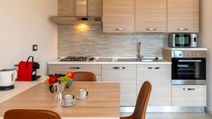 Una cocina moderna con armarios de madera clara, estufa de acero inoxidable, microondas y horno empotrado.
