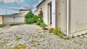 A residential building with a gravel driveway, a white door, and a small garden with red and yellow flowers. - Maisonneuve by Interhome (Ile d'Oléron)