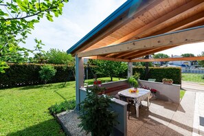 An outdoor patio area with a wooden pergola, a table with chairs, and potted plants. - Apartment Jani (Istria - Poreč) (Poreč)
