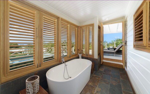 A bathroom with a freestanding bathtub, wooden shutters on the windows, and a view of a pool and outdoor seating. - Stunning Retreat with Pool and Sunset Views - Northlight (Holders)