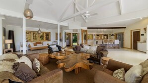 A spacious living area with a high ceiling, wooden furniture, and a view into the kitchen.