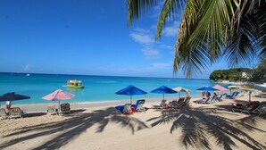 A beach with sun loungers and umbrellas, a boat in the water, and a clear blue sky. - Stunning Retreat with Pool and Sunset Views - Northlight (3 bed) (Holders)