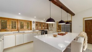 A modern kitchen with white cabinetry, a large island, pendant lighting, and wooden accents. - Stunning Retreat with Pool and Sunset Views - Northlight (3 bed) (Holders)