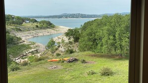 Blick auf einen See mit steiniger Uferlinie und einer Wiese mit einem Kanu und einem Holzstoß.