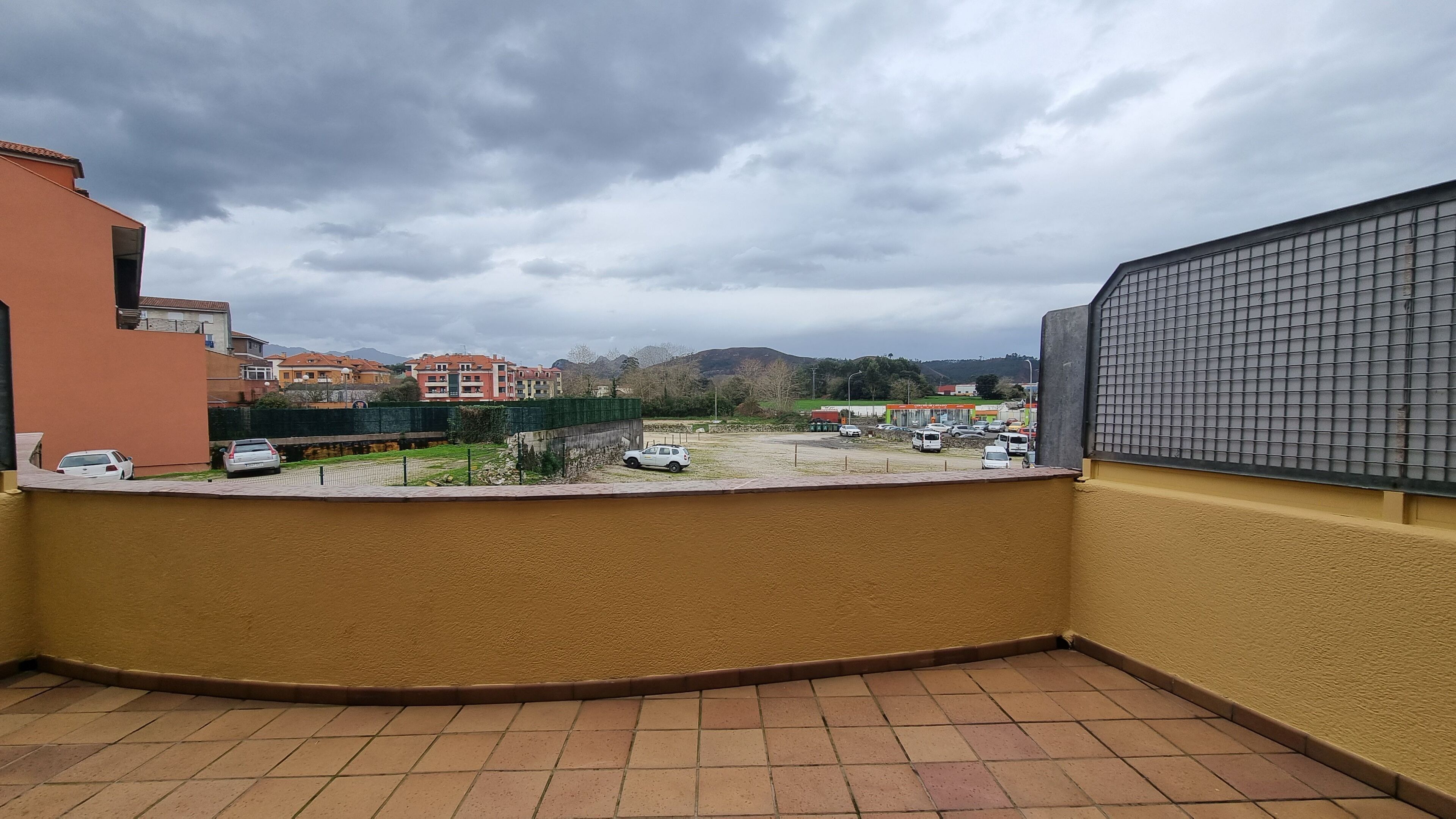 Un balcon donnant sur un parking et sur des bâtiments situés au loin.