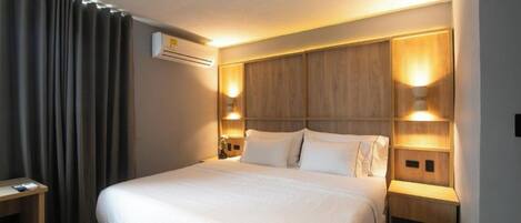 Une chambre d’hôtel avec un grand lit, deux tables de chevet, un bureau et un climatiseur fixé au mur.