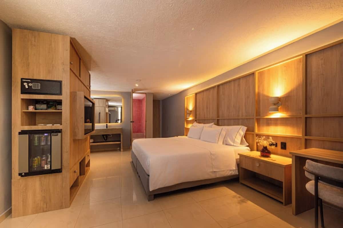 Quarto de hotel moderno com uma cama grande, guarda-roupa de madeira, televisão embutida e uma pequena cozinha equipada.