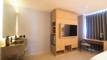 Quarto de hotel moderno com televisão integrada, escrivaninha com cadeira, janela grande com cortinas e lavatório de cimento.