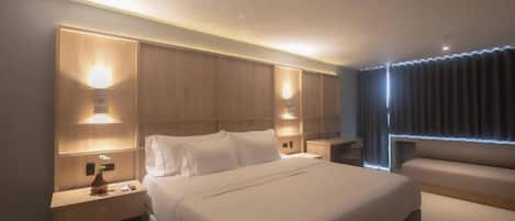 A modern hotel room with a large bed, bedside tables with lamps, a seating area, and a view of the city through the window.