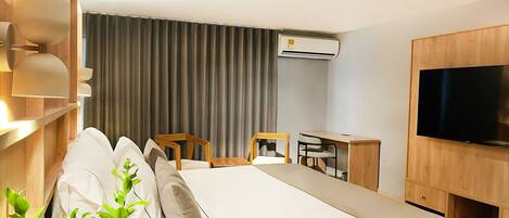 A hotel room with a bed, a desk, a chair, a television, and an air conditioning unit.