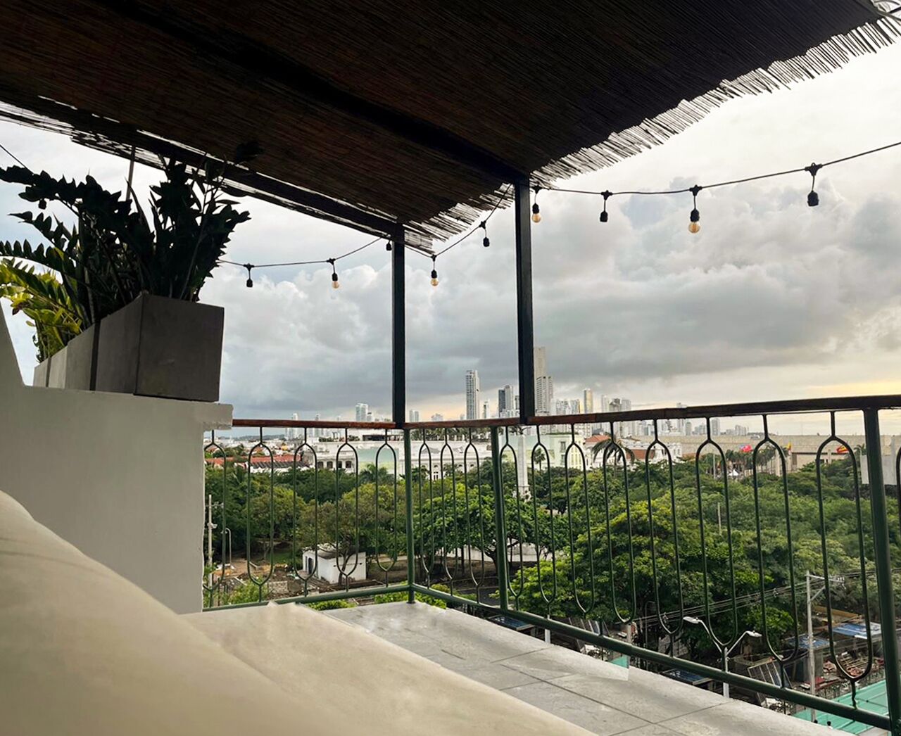 A balcony with a view of a cityscape, a railing, and string lights.